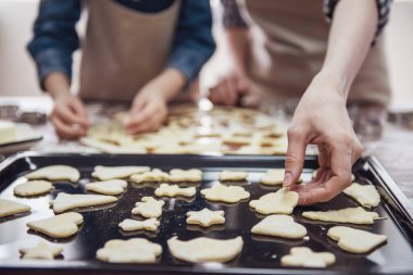 Küçük kız ve annesi mutfakta çerez kesici kullanarak çerezleri hazırlamak önlük içinde kırpılmış görüntü
