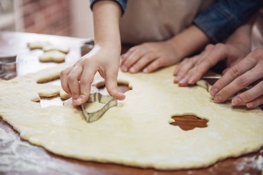 Küçük kız ve annesi mutfakta çerez kesici kullanarak çerezleri hazırlamak önlük içinde kırpılmış görüntü