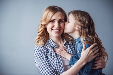 Sevimli küçük kız ve güzel genç annesi gri arka plan üzerinde. Kız annesi yanak içinde öpüşme