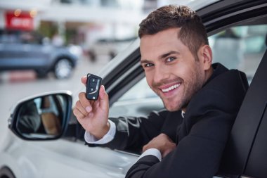 Takım elbiseli yakışıklı işadamı göstermek bir anahtar, kameraya bakıyor ve araba Bayilik yeni arabada otururken gülümseyen