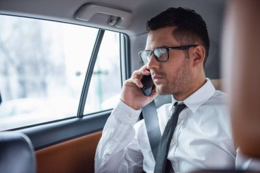 Takım elbise ve gözlük yakışıklı işadamı arabanın arka koltukta otururken cep telefonla konuşuyor