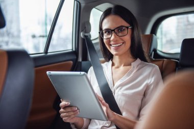 Gözlük güzel kadın dijital tablet kullanma ve arabanın arka koltukta otururken gülümseyen
