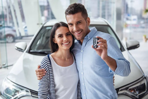 Visiting car dealership. Beautiful couple is holding a key of their new car, looking at camera and smiling
