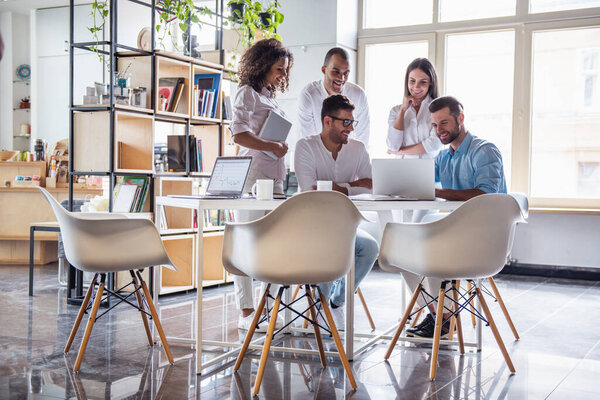 Successful young business people are using gadgets, sharing ideas and smiling while working in office