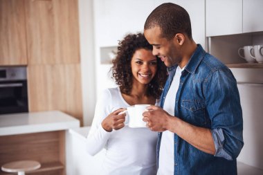 Güzel bir çift kahve içiyor, mutfakta dinlenirken sarılıyor ve gülümsüyor.