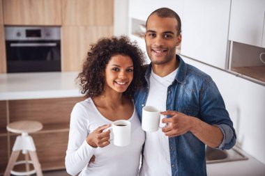 Güzel bir çift kahve içiyor, mutfakta dinlenirken sarılıyor ve gülümsüyor.
