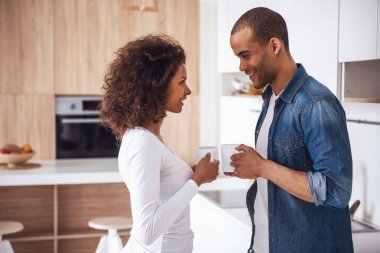 Güzel bir çift kahve içiyor, birbirlerine bakıyor ve mutfakta dinlenirken gülümsüyor.