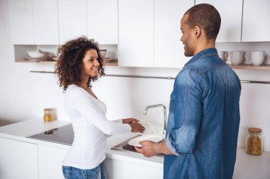 Güzel bir çift mutfakta bulaşıkları yıkarken konuşuyor ve gülümsüyor.