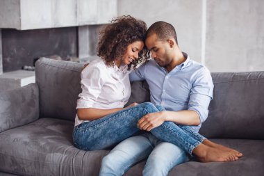 Güzel, genç bir çift evdeki kanepede otururken sarılıp gülümsüyor.