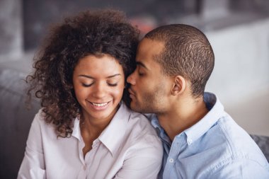 Güzel, genç bir çift evdeki kanepede otururken sarılıp gülümsüyor.