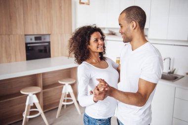 Güzel genç çift mutfakta dans ederken gülümsüyor.