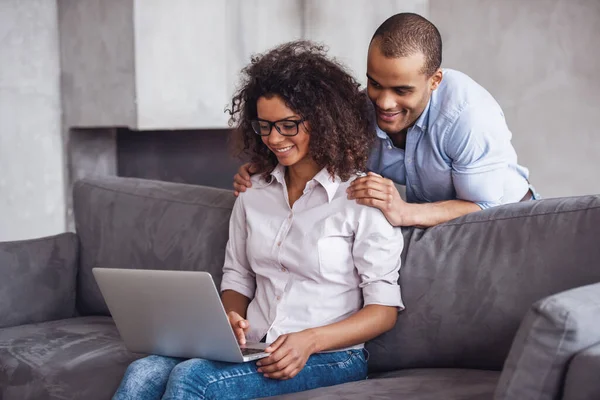 Beautiful young couple on couch at home. Business woman is using a laptop while her boyfriend is doing her massage