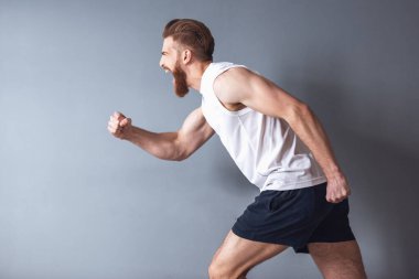 Çalışan ve çığlık, gri arka plan üzerinde yakışıklı genç sakallı sporcu yan görünüm