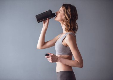 Güzel genç sporcumuz Spor beslenme, gri arka plan üzerinde içiyor
