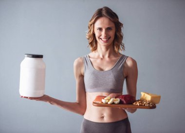 Güzel genç sporcumuz bir şişeyle Spor beslenme ve sağlıklı gıda ile ahşap tepsi gri arka plan üzerinde tutuyor