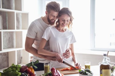 Güzel genç çift evde mutfakta sağlıklı yemekler pişirirken konuşuyor ve gülümsüyor.