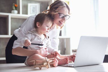 Güzel iş anne bir dizüstü bilgisayar kullanarak ve onun sevimli bebek çocuk evde vakit ise gülümseyen