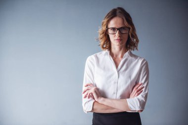 Gözlük güzel kadın kamera duran gri arka plan üzerinde çapraz silah ile bakıyor