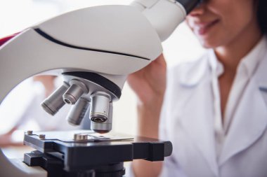 Güzel tıp doktoru bir mikroskop kullanarak ve laboratuarda çalışırken gülümseyen