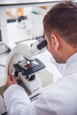 Yakışıklı tıp doktoru laboratuarda çalışırken bir mikroskop kullanarak