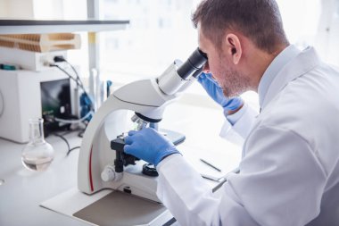 Yakışıklı tıp doktoru laboratuarda çalışırken bir mikroskop kullanarak