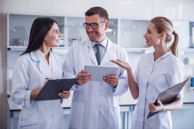Güzel tıp doktorları dijital tablet kullanarak, test sonuçlarını tartışıyor ve laboratuarda çalışırken gülümseyen