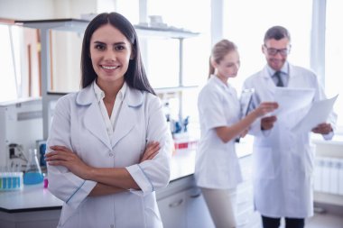 Laboratuarda. Güzel tıp doktoru kameraya bakıyor ve gülümsüyor, iş arkadaşları içinde belgili tanımlık geçmiş