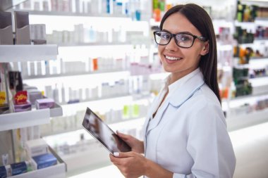 Güzel kadın eczacı dijital tablet kullanma, kameraya bakıyor ve eczanede çalışırken gülümseyen