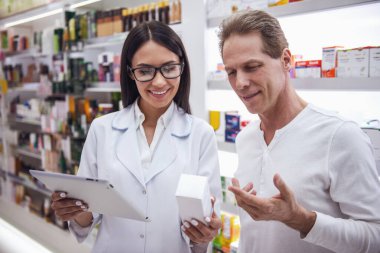 Güzel genç kadın eczacı bir ilaç dijital tablet tutarak ve gülümseyen bir istemciye eczaneden, öne sürüyor