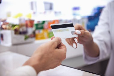 Eczanede. Genç kadın eczacı nakit masa başında çalışırken bir istemciden bir kredi kartı alarak Resim kırpılmış