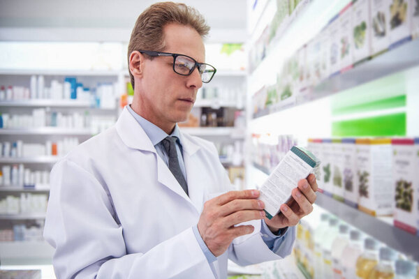 Handsome pharmacist in eyeglasses is checking medication in pharmacy