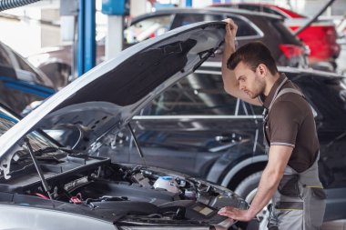 Üniformalı yakışıklı genç otomatik mekanik Oto Servisi arabaya incelenmesi