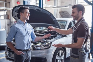 Otomatik hizmetinde. Üniformalı yakışıklı genç otomatik mekanik araba anahtarı bir istemciye geri dönüyor, hem de gülüyorsun