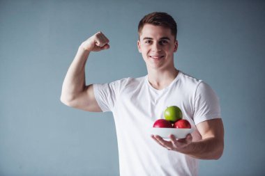 Yakışıklı adam meyve tutan kasları gösterilen, kameraya bakarak ve, gri arka plan üzerinde gülümseyen