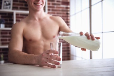 Çıplak gövde ile yakışıklı kaslı adam kendini süt dökme ve evde mutfakta dururken gülümseyen