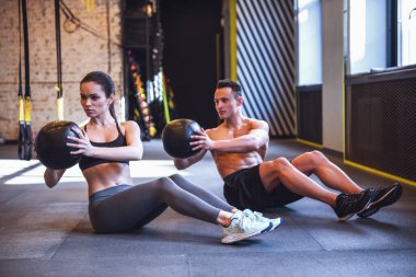 Güzel genç spor çifti jimnastik salonunda sağlık topuyla antrenman yapıyor.