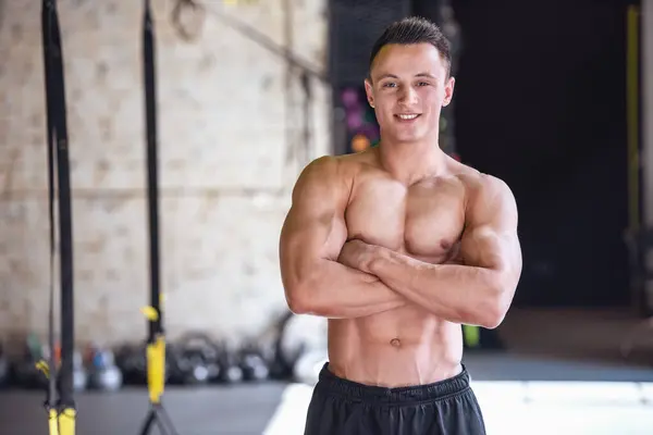 英俊的年轻肌肉型男是望着相机 微笑着站在一起在健身房的双臂交叉 — 图库照片