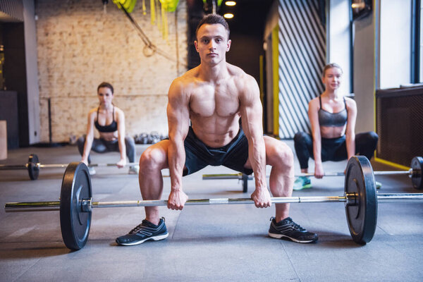 Beautiful young sports people are working out with barbells in gym