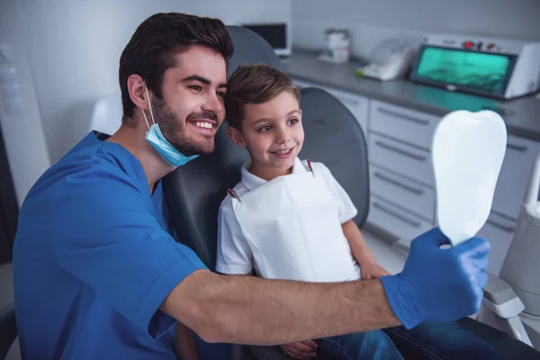 Little boy is sitting in chair and smiling while visiting a dentist