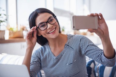 Kahve içme ve selfie yapmak için bir telefon kullanarak bir kafede oturan genç güzel iş kadını