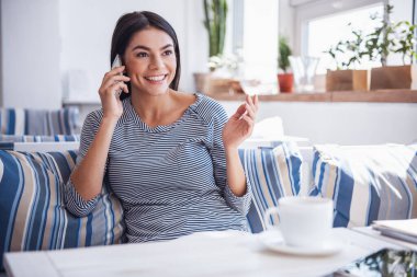 Neşeli genç güzel kız bir kafede oturan ve kahve içme telefonda konuşurken duygusal.