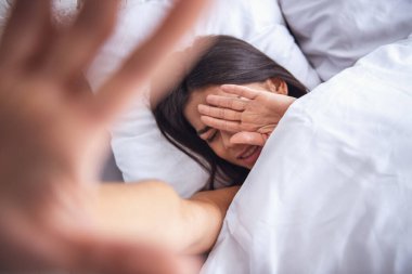 Üstten Görünüm. Utangaç genç güzel kız yüzünü, evde bir yatak odasında bir yatakta uyanmayı gizler