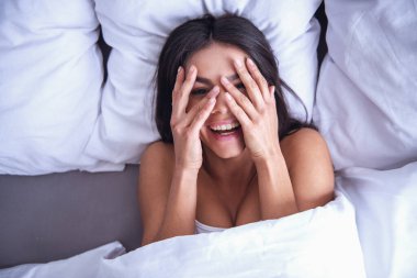 Üstten Görünüm. Utangaç genç güzel kız yüzünü, evde bir yatak odasında bir yatakta uyanmayı gizler