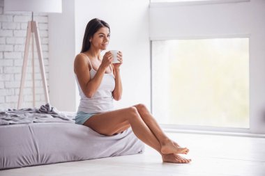 Günaydın! Mutlu genç güzel kadın yatak odasında çay veya kahve evde içme.