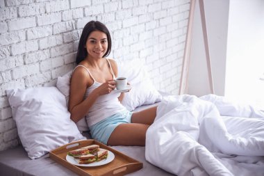 Günaydın! Mutlu genç güzel kadın yatakta evde otururken Kahvaltı