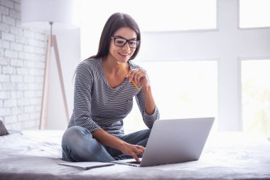 Ev ofis. Dizüstü bilgisayarda çalışan yatağın üstüne oturan kadın.