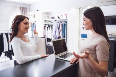 Güzel kadın tezgâhtar çekici kadın istemciye konuşuyor ve butik olarak kasada dururken gülümseyen