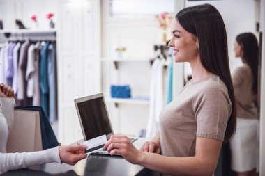 Güzel kadın tezgâhtar kredi kartı alarak, bir istemciye konuşuyor ve butik olarak kasada dururken gülümseyen