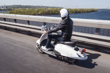 Deri ceket ve kask adam Şehir Köprüsü aracılığıyla scooter üzerinde sürme