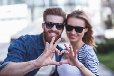 Güzel genç bir çift güneş gözlüğü, sarılma, kalp gösterilen ve açık havada duran süre gülümseyen